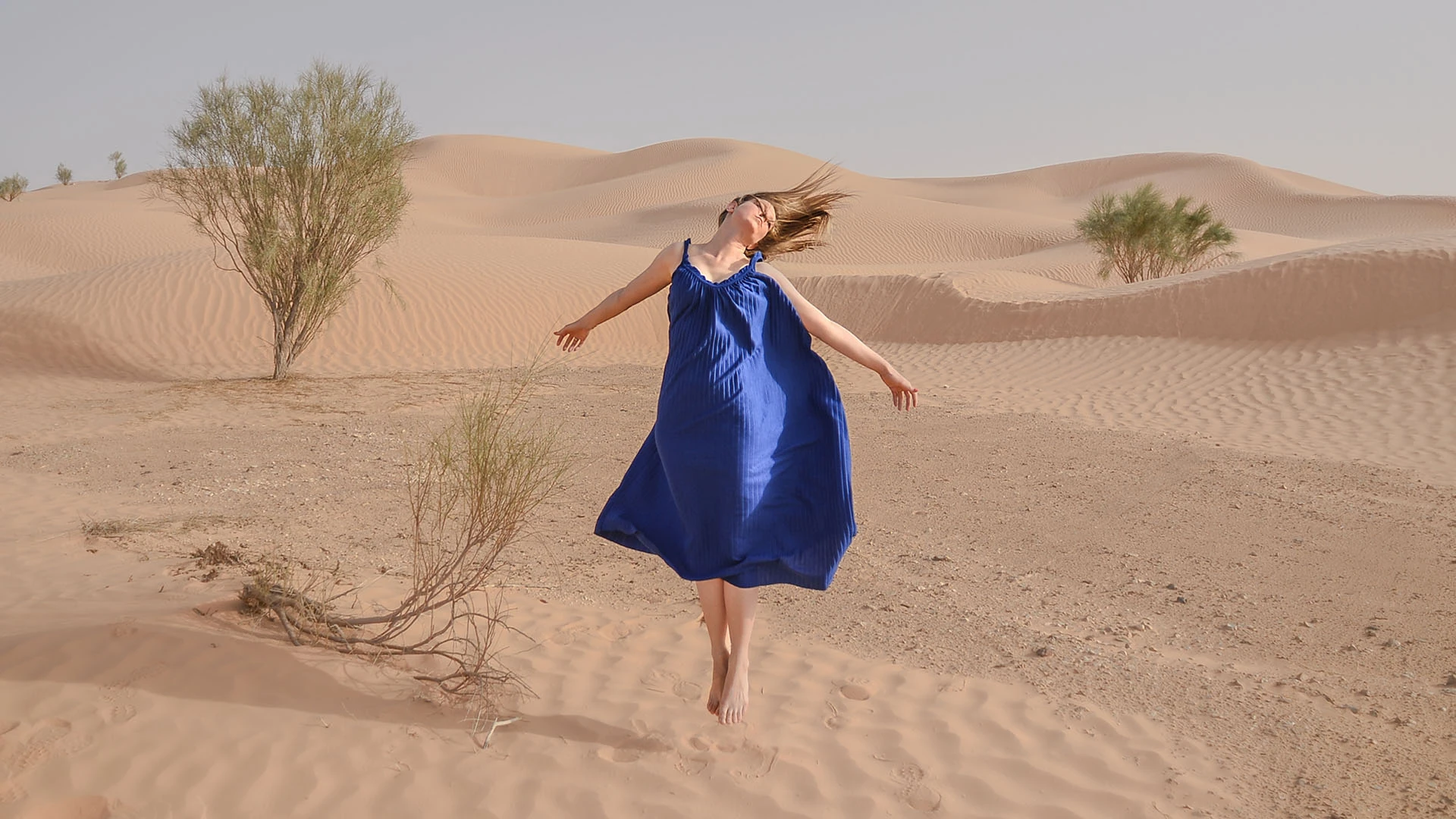 A woman in a blue dress suspended above the desert sand, photographed by Péter Kálló