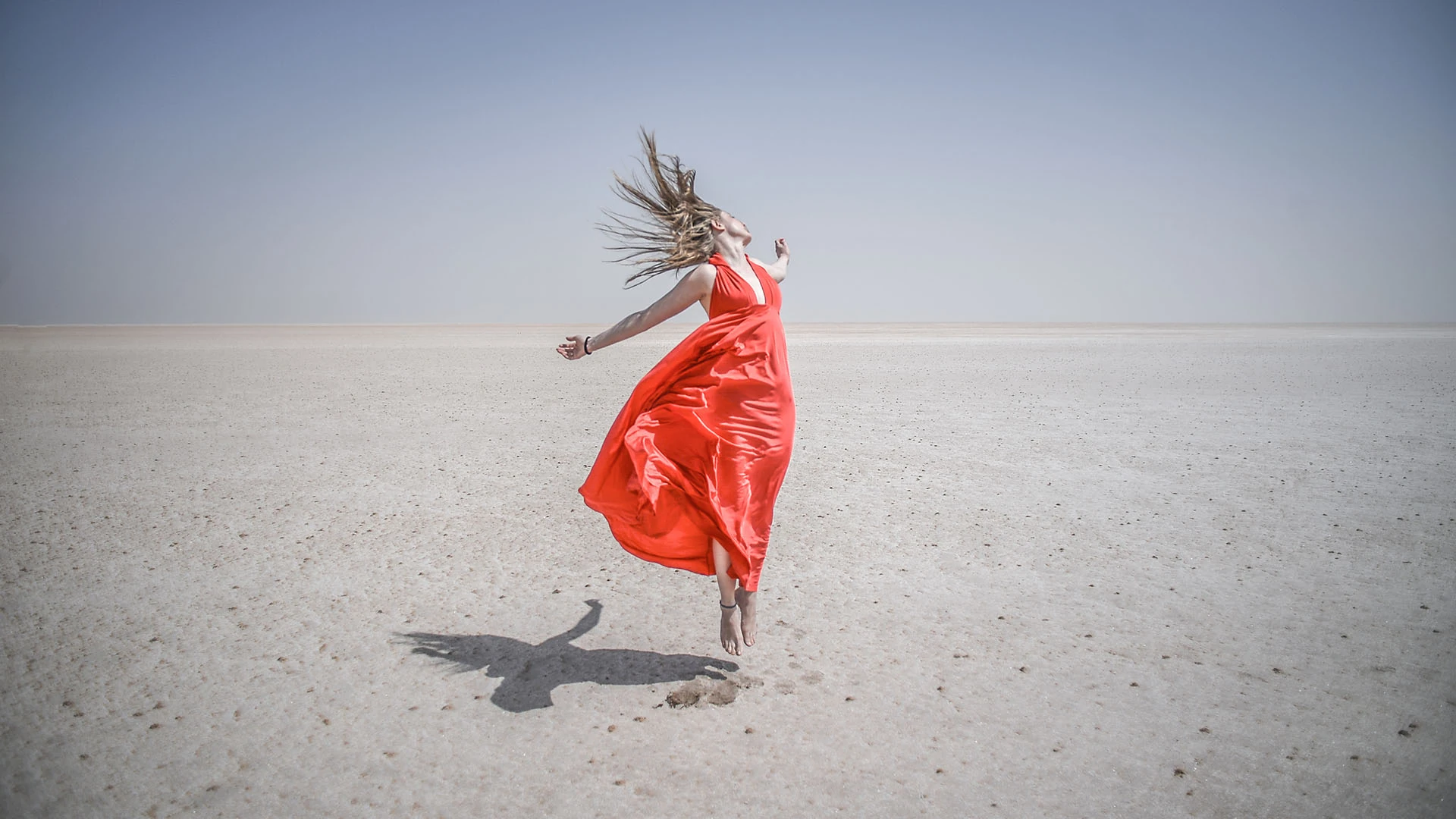 A woman in a red dress floating above a vast empty desert, photographed by Péter Kálló